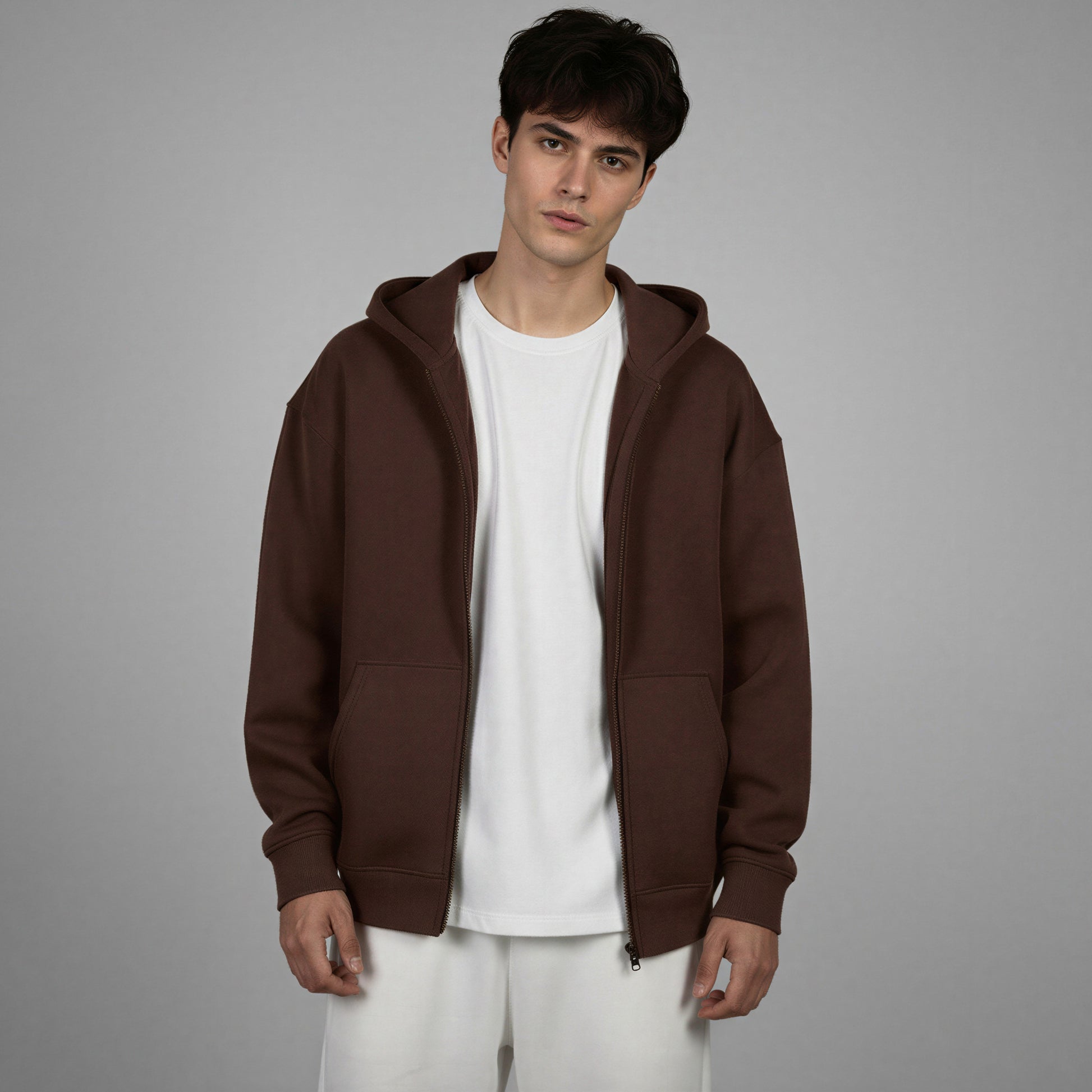 Man wearing a brown hoodie over a white shirt on a gray background