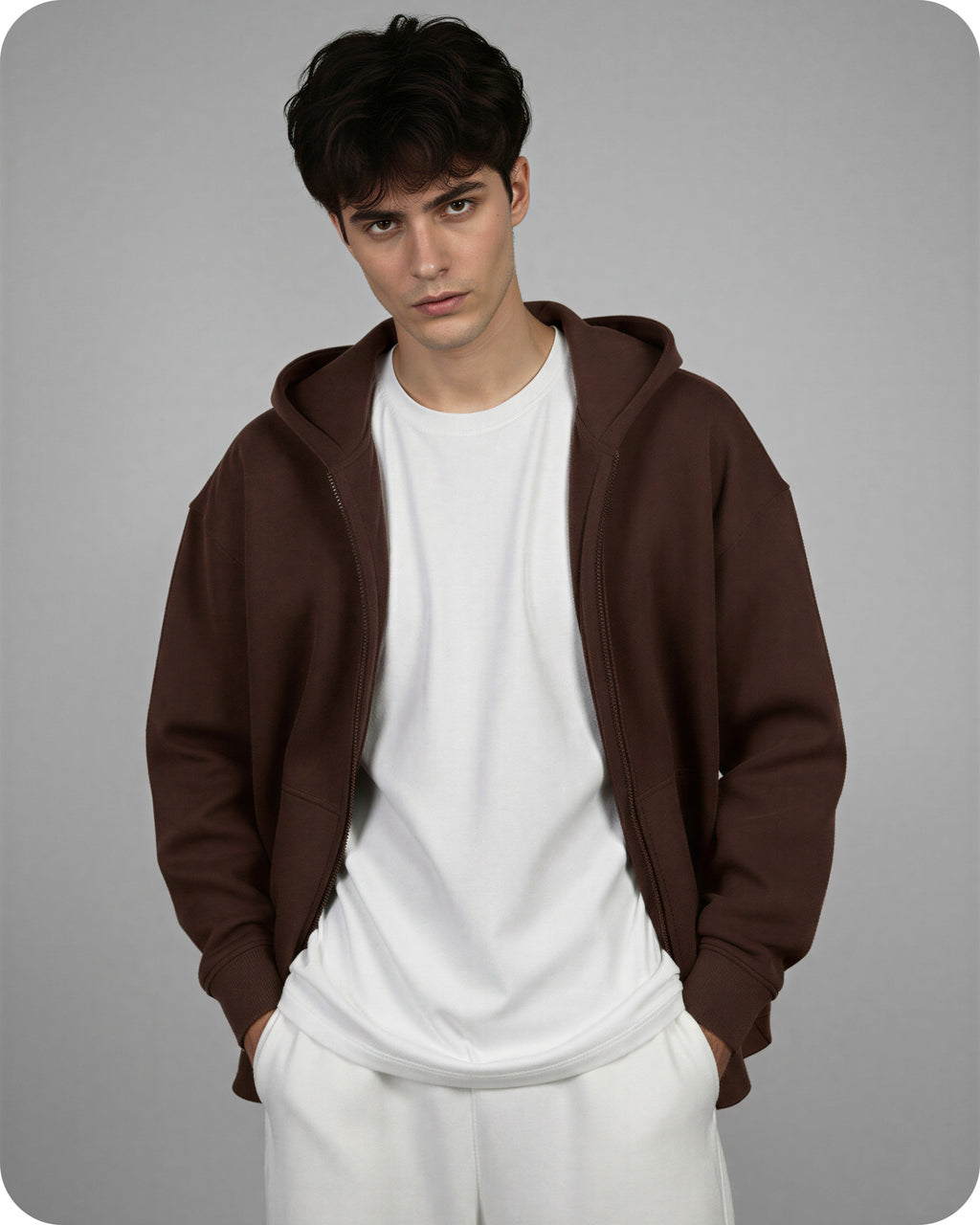 Man wearing a brown hoodie over a white shirt and pants on a gray background