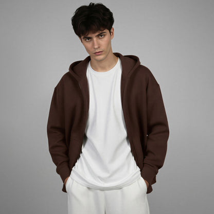 Man wearing a brown hoodie over a white shirt and pants on a gray background