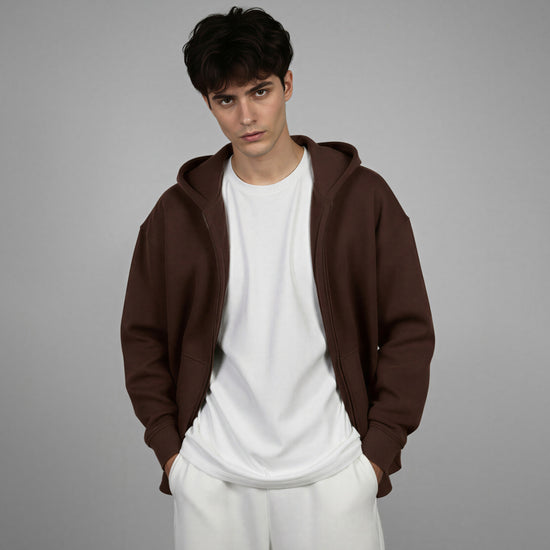 Man wearing a brown hoodie over a white shirt and pants on a gray background