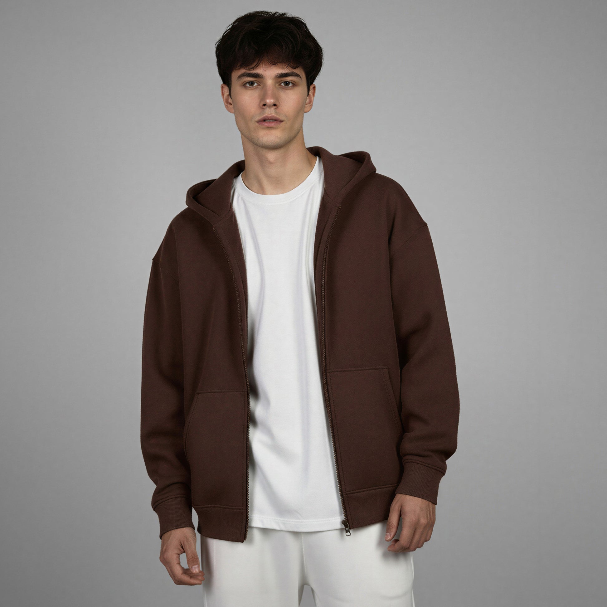 Man wearing a brown hoodie over a white shirt on a gray background
