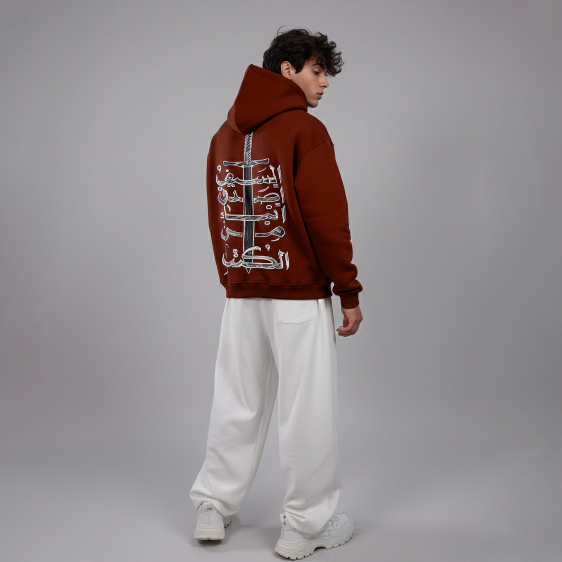 Person wearing a brown hoodie with Arabic text on the back against a gray background