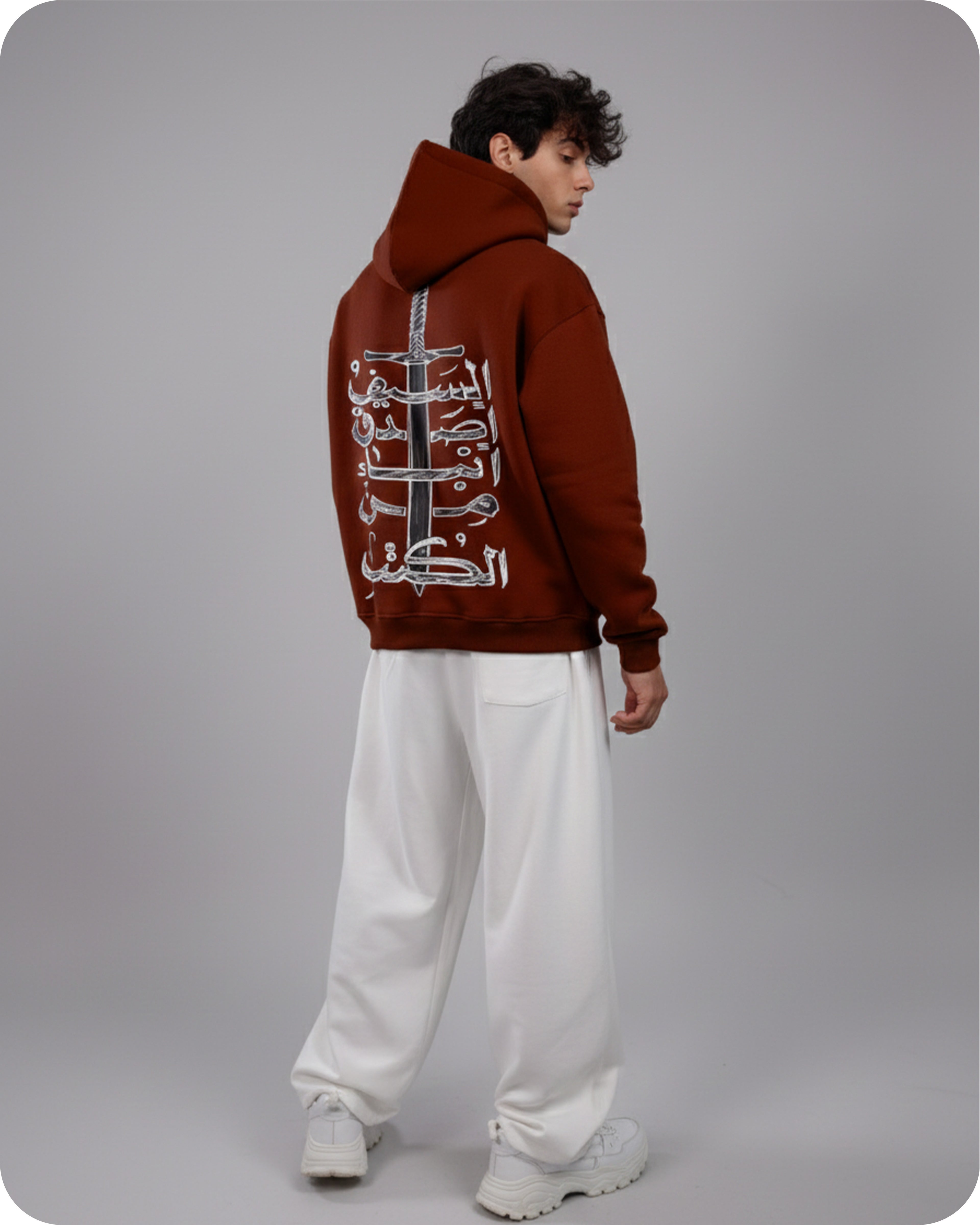 Person wearing a brown hoodie with Arabic text on the back against a gray background