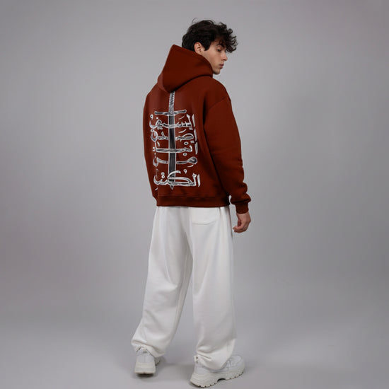 Person wearing a brown hoodie with Arabic text on the back against a gray background