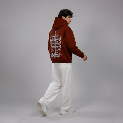 Person wearing a brown hoodie with white text on the back, standing against a gray background