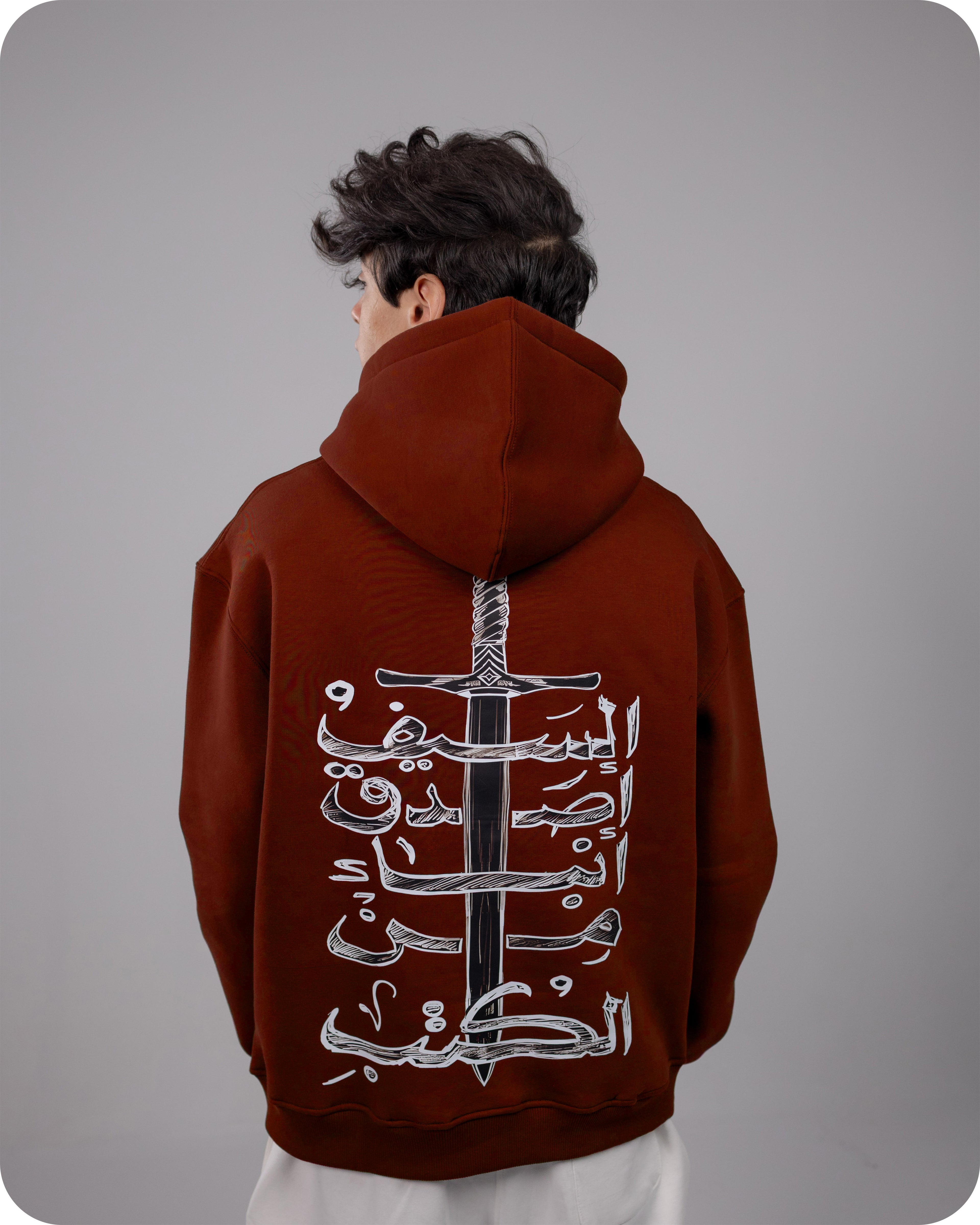 Person wearing a Burgundy hoodie with Arabic text and a sword design on the back against a gray background