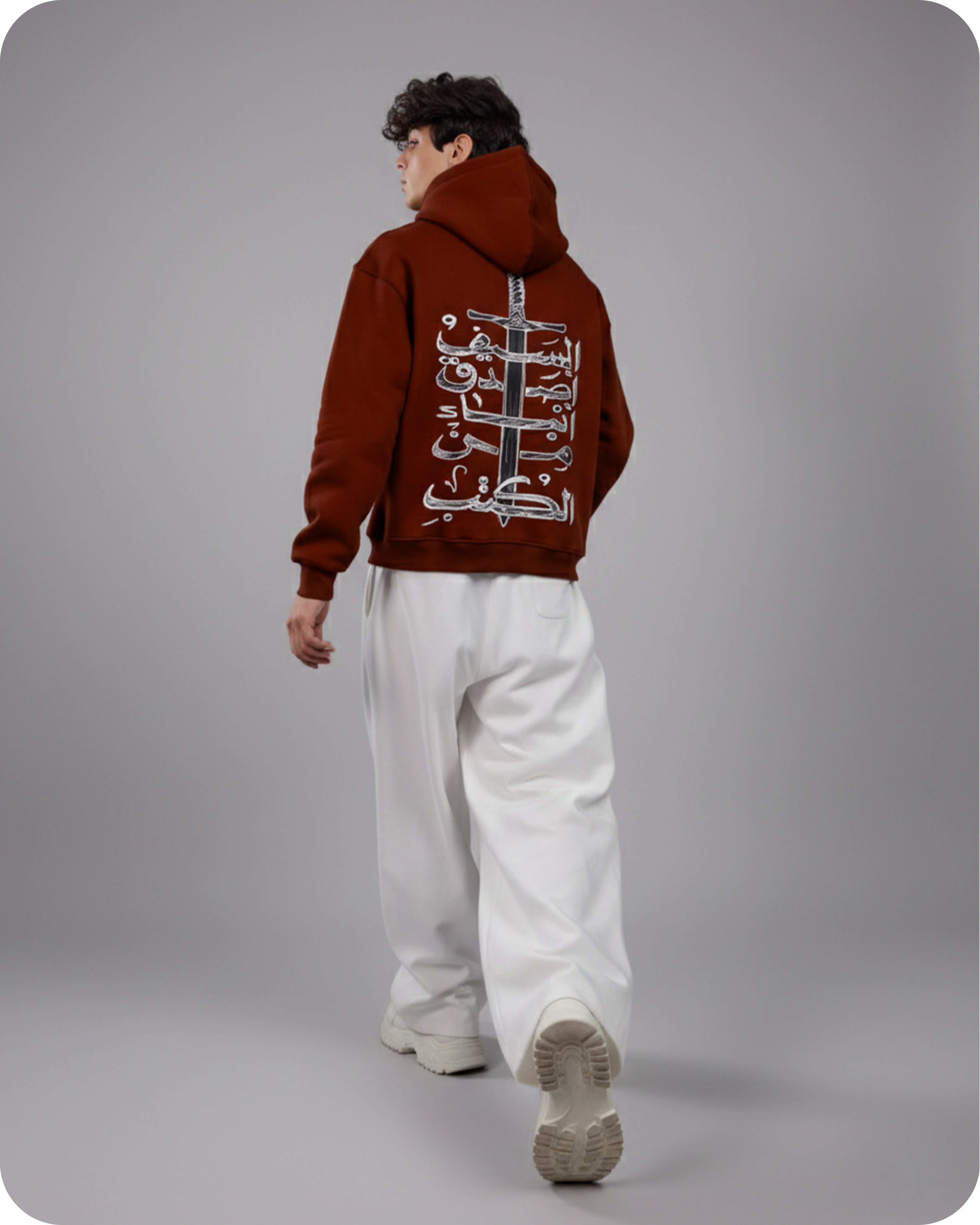 Person wearing a brown hoodie with text on the back, standing against a gray background