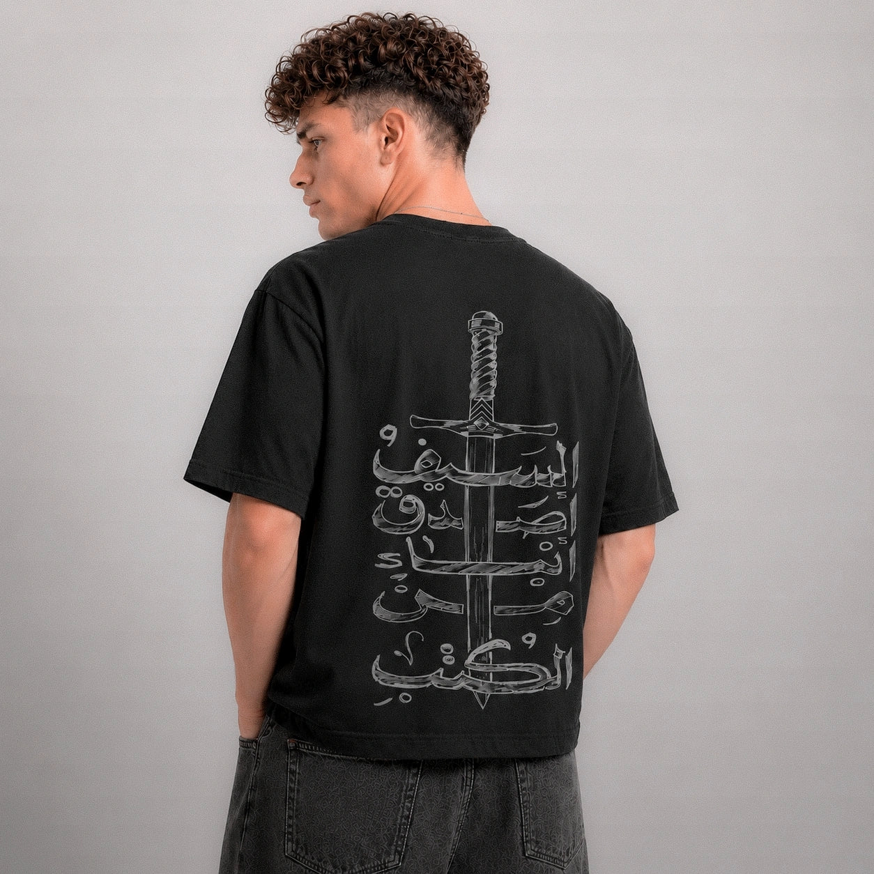 Person wearing a black t-shirt with a white graphic design on the back against a gray background
