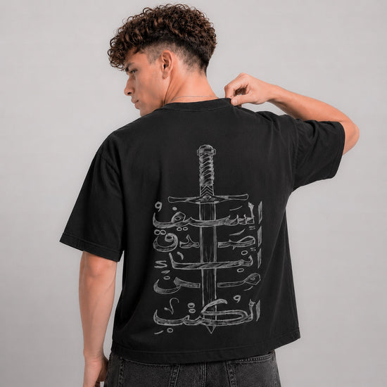 Person wearing a black t-shirt with a sword design on the back against a gray background