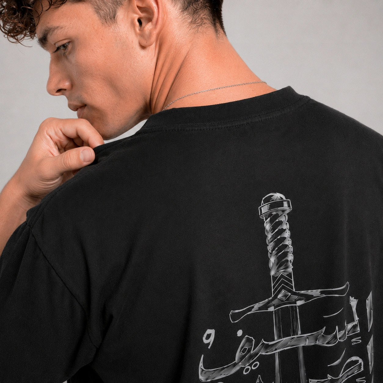 Man wearing a black t-shirt with a sword design on the back, looking over his shoulder.