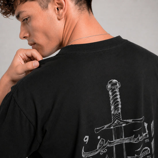 Man wearing a black t-shirt with a sword design on the back, looking over his shoulder.