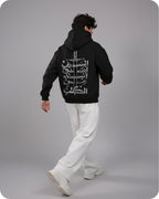 Person wearing a black hoodie with white graphic design on the back, standing against a gray background