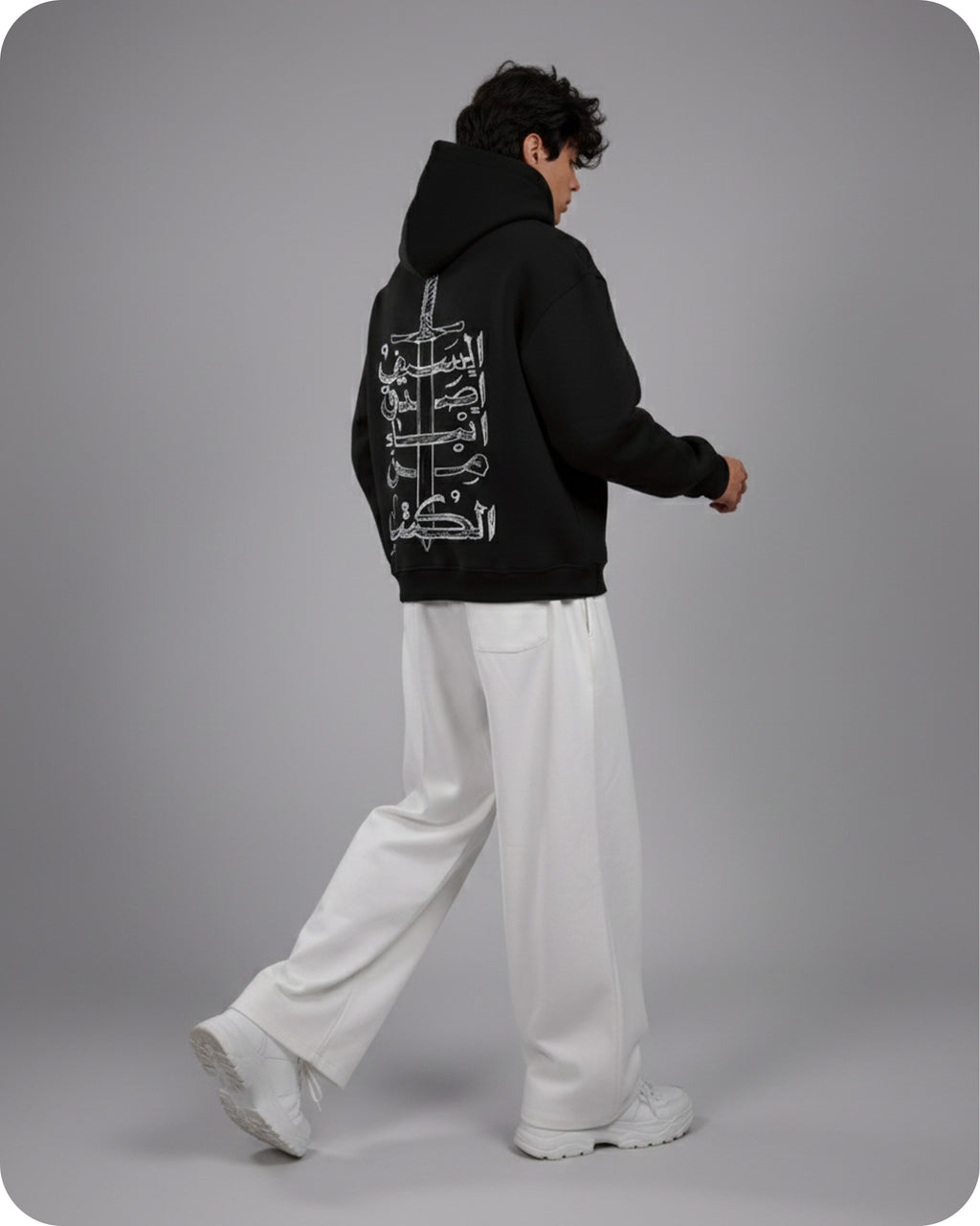 Person wearing a black hoodie with white text on the back, standing against a gray background