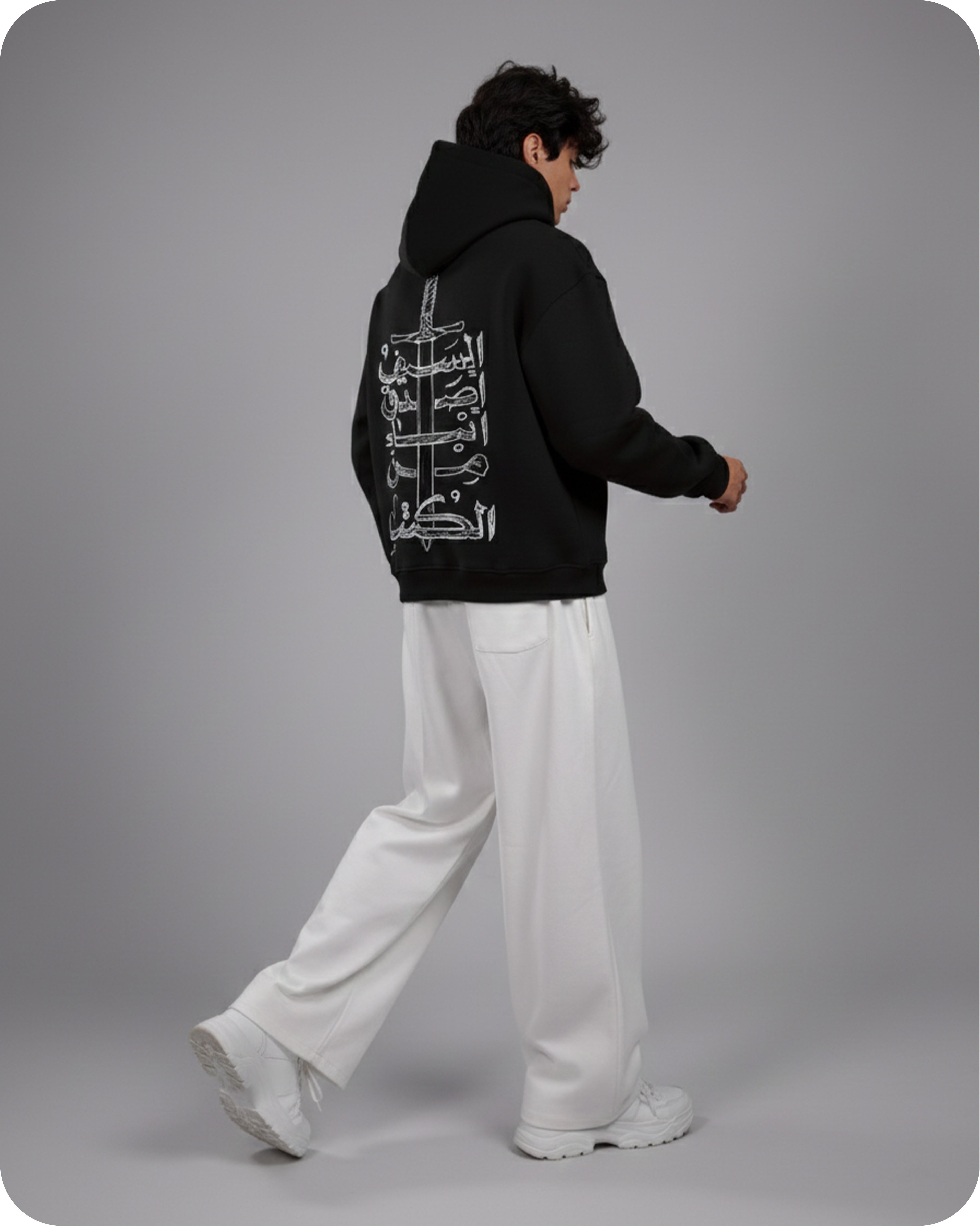 Person wearing a black hoodie with white text on the back, standing against a gray background