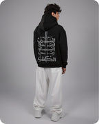 Person wearing a black hoodie with white graphic design on the back, standing against a gray background