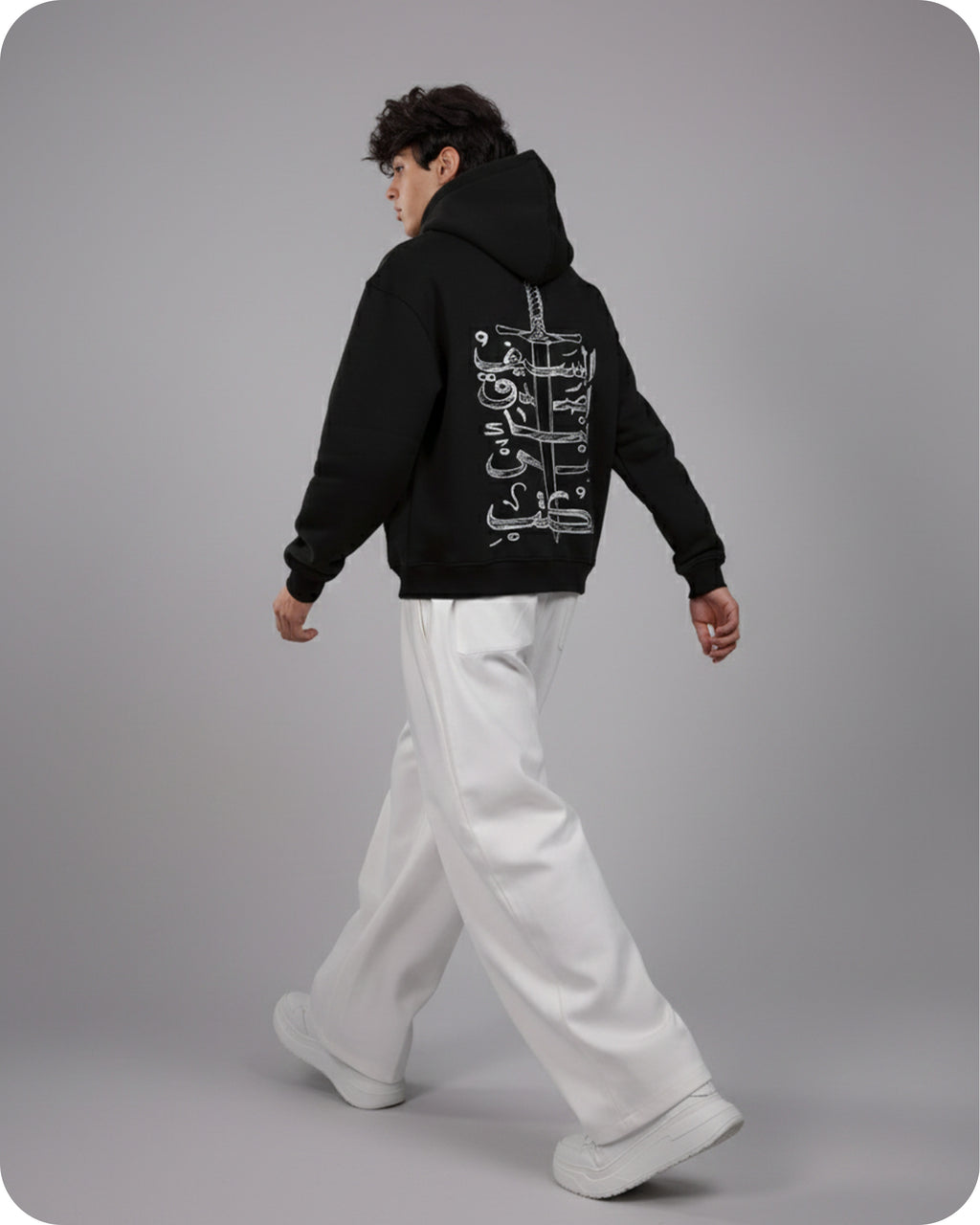 Person wearing a black hoodie with white text on the back, standing against a gray background