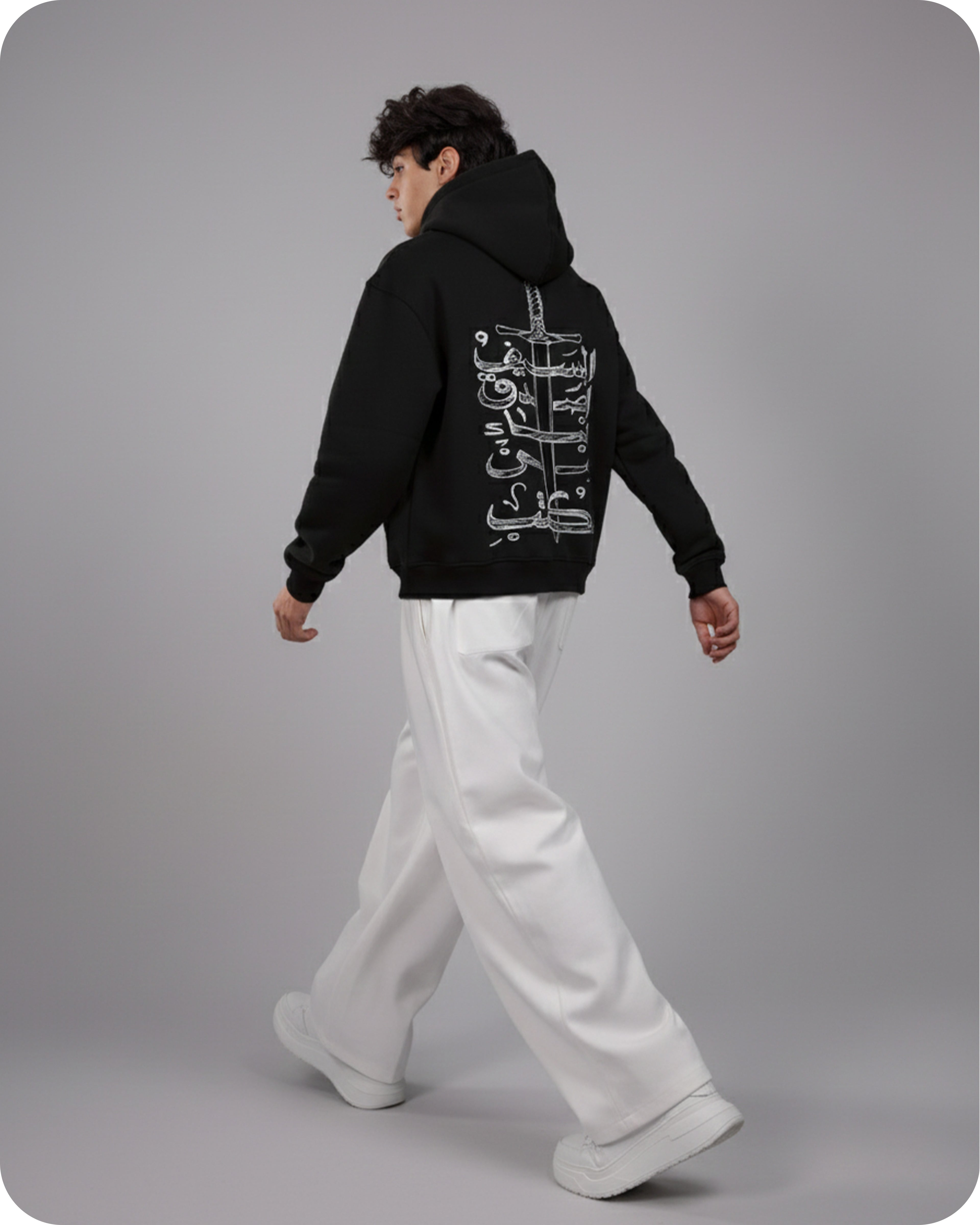 Person wearing a black hoodie with white text on the back, standing against a gray background