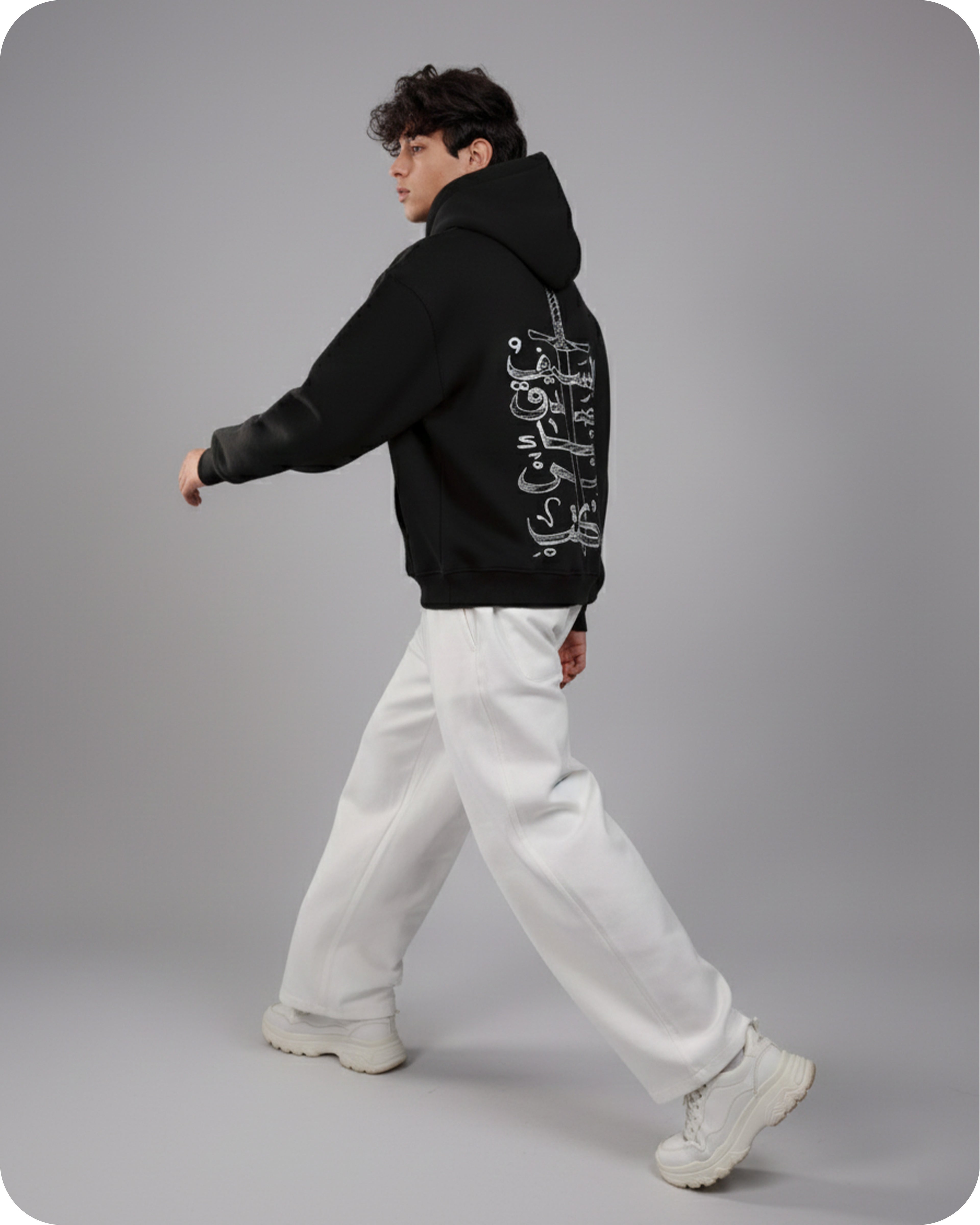 Person wearing a black hoodie with white text and white pants on a gray background