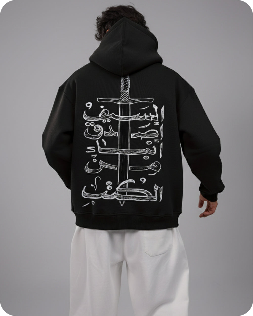 Person wearing a black hoodie with white Arabic calligraphy and sword design on the back, standing against a gray background.