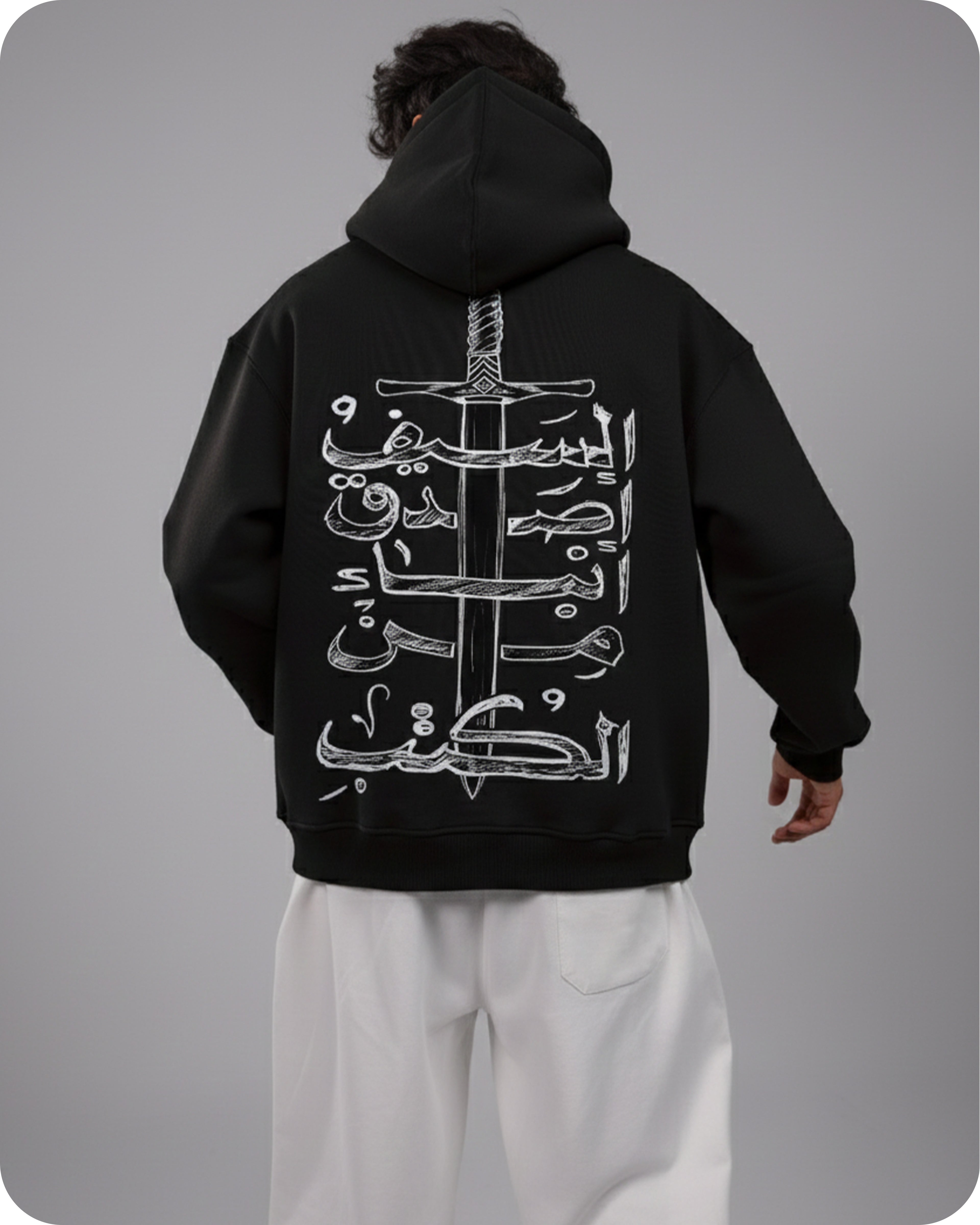 Person wearing a black hoodie with white Arabic calligraphy and sword design on the back, standing against a gray background.