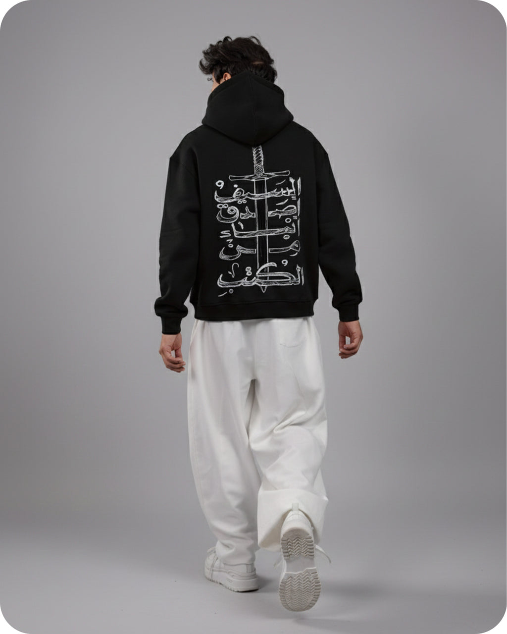 Person wearing a black hoodie with white Arabic text on the back against a gray background