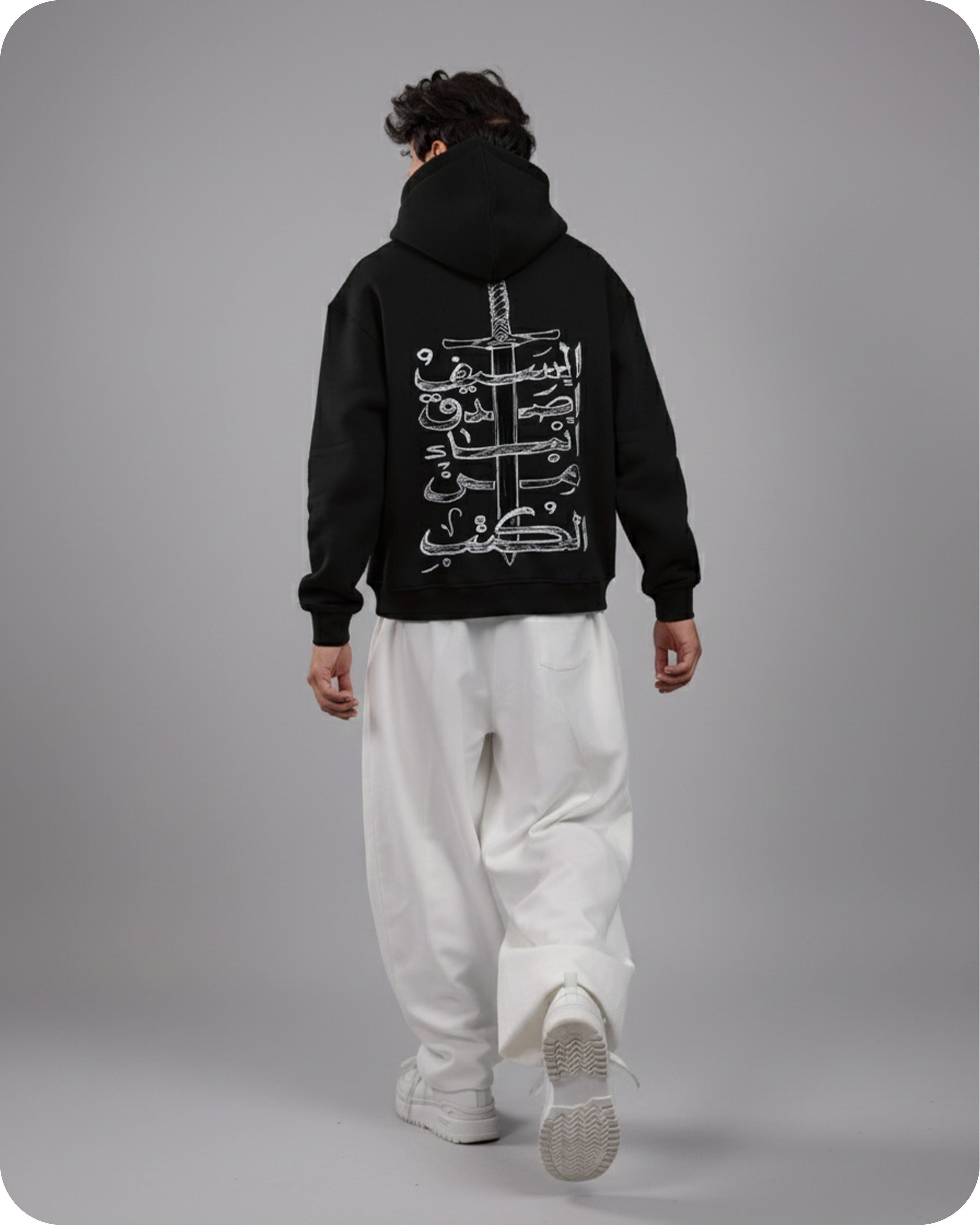 Person wearing a black hoodie with white Arabic text on the back against a gray background