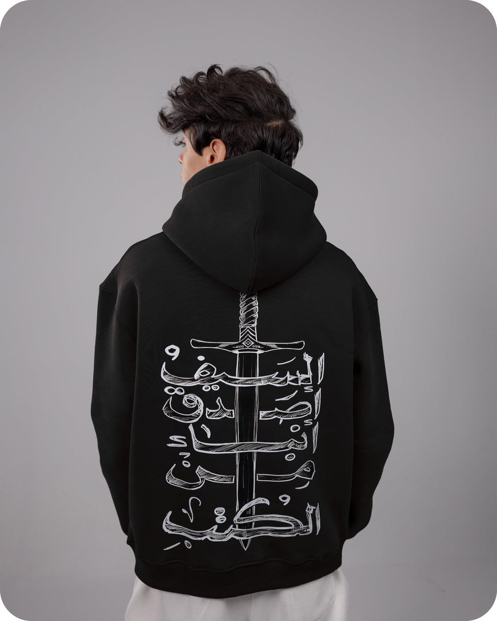 Person wearing a black hoodie with white Arabic calligraphy design on the back against a gray background
