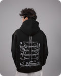 Person wearing a black hoodie with white Arabic calligraphy design on the back against a gray background