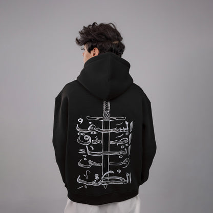 Person wearing a black hoodie with white Arabic calligraphy design on the back against a gray background