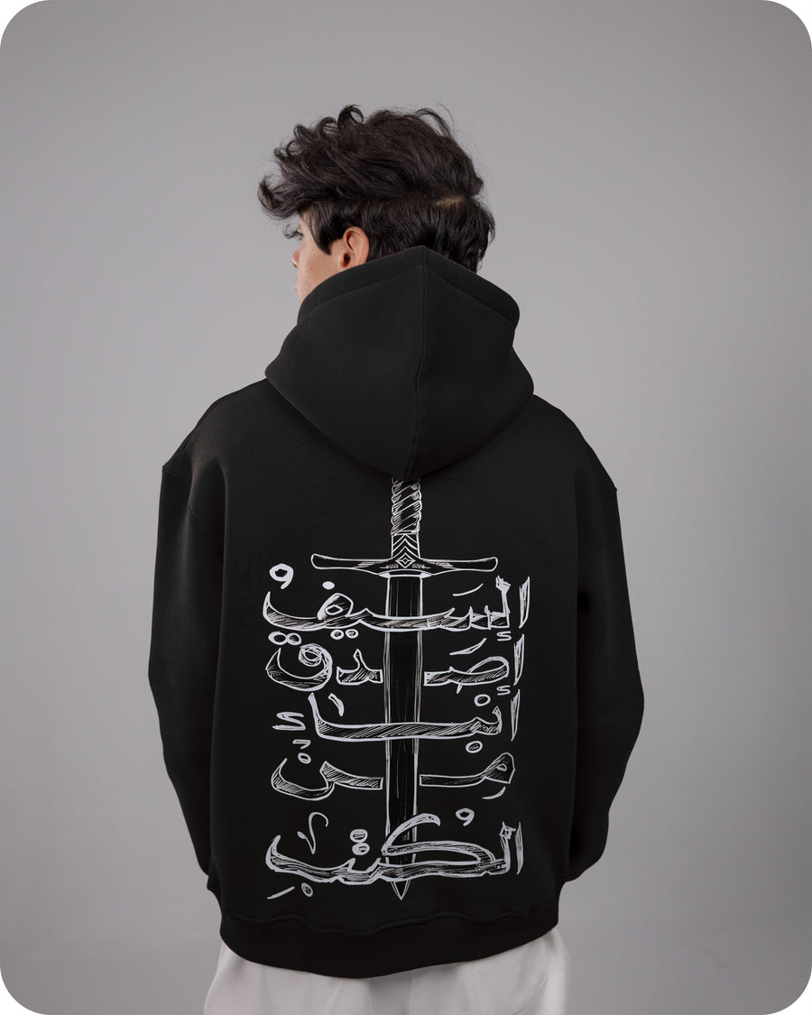 Person wearing a black hoodie with white Arabic calligraphy design on the back against a gray background