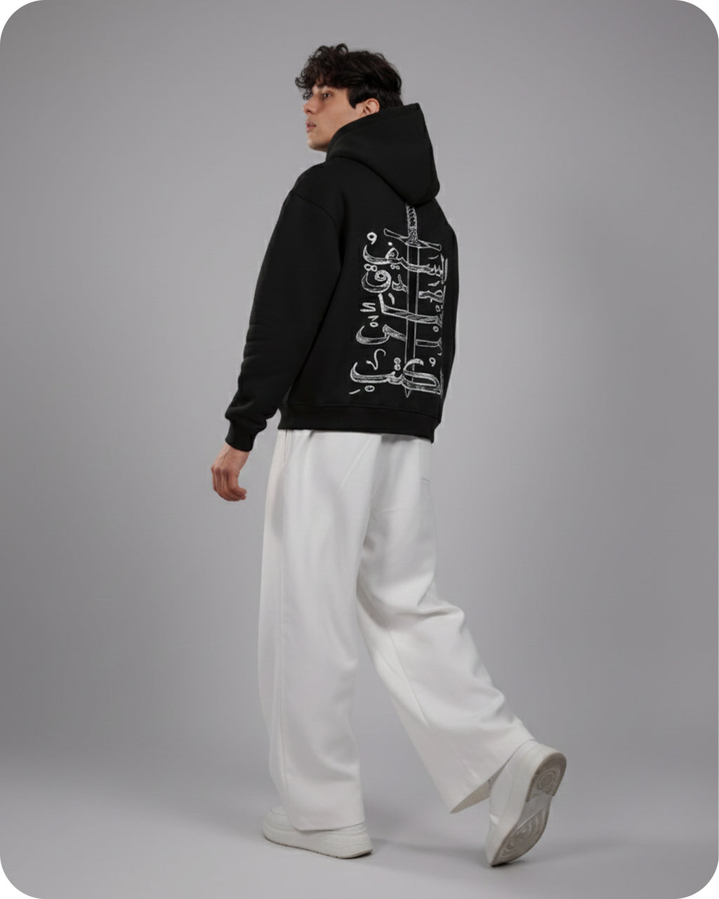 Person wearing a black hoodie with white text and white pants on a gray background