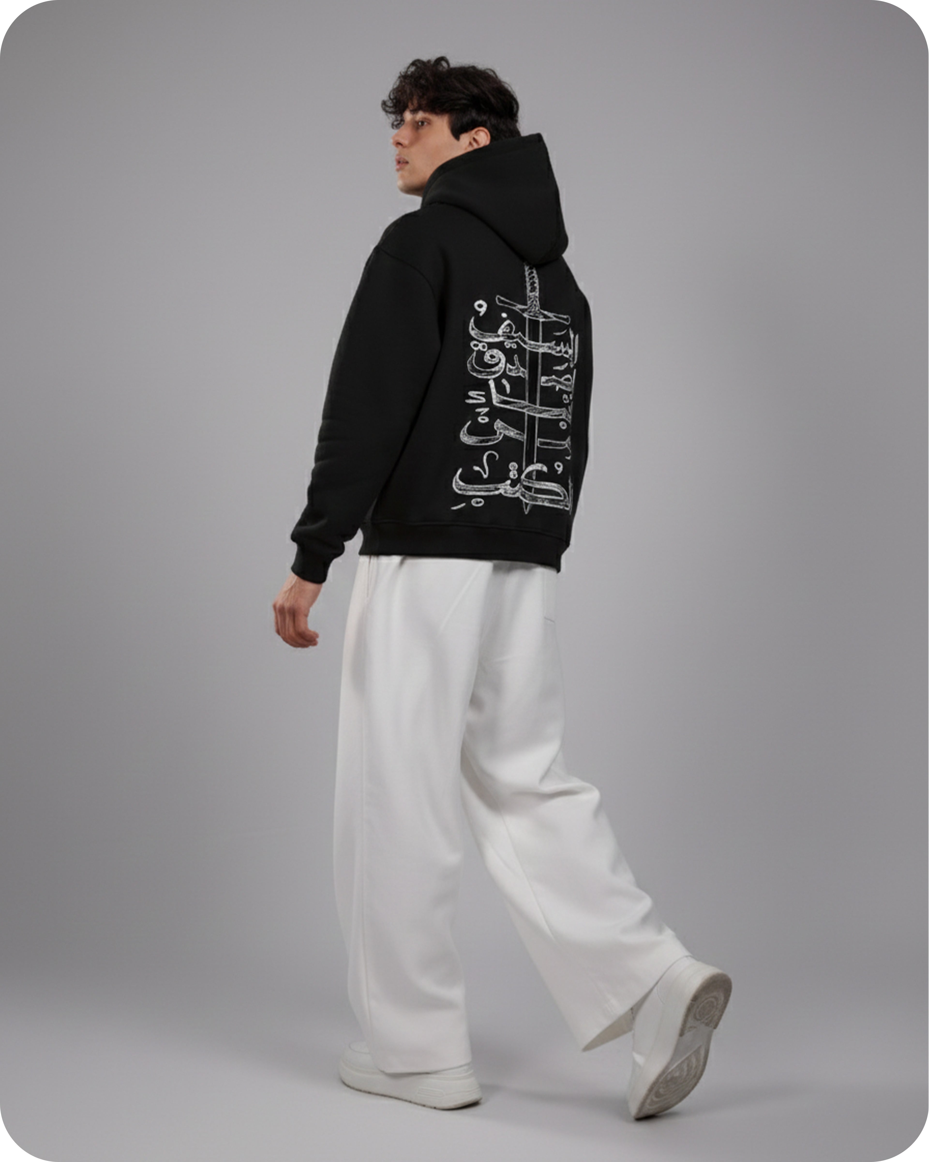 Person wearing a black hoodie with white text and white pants on a gray background