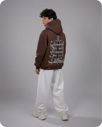 Person wearing a brown hoodie with Arabic text on the back against a gray background