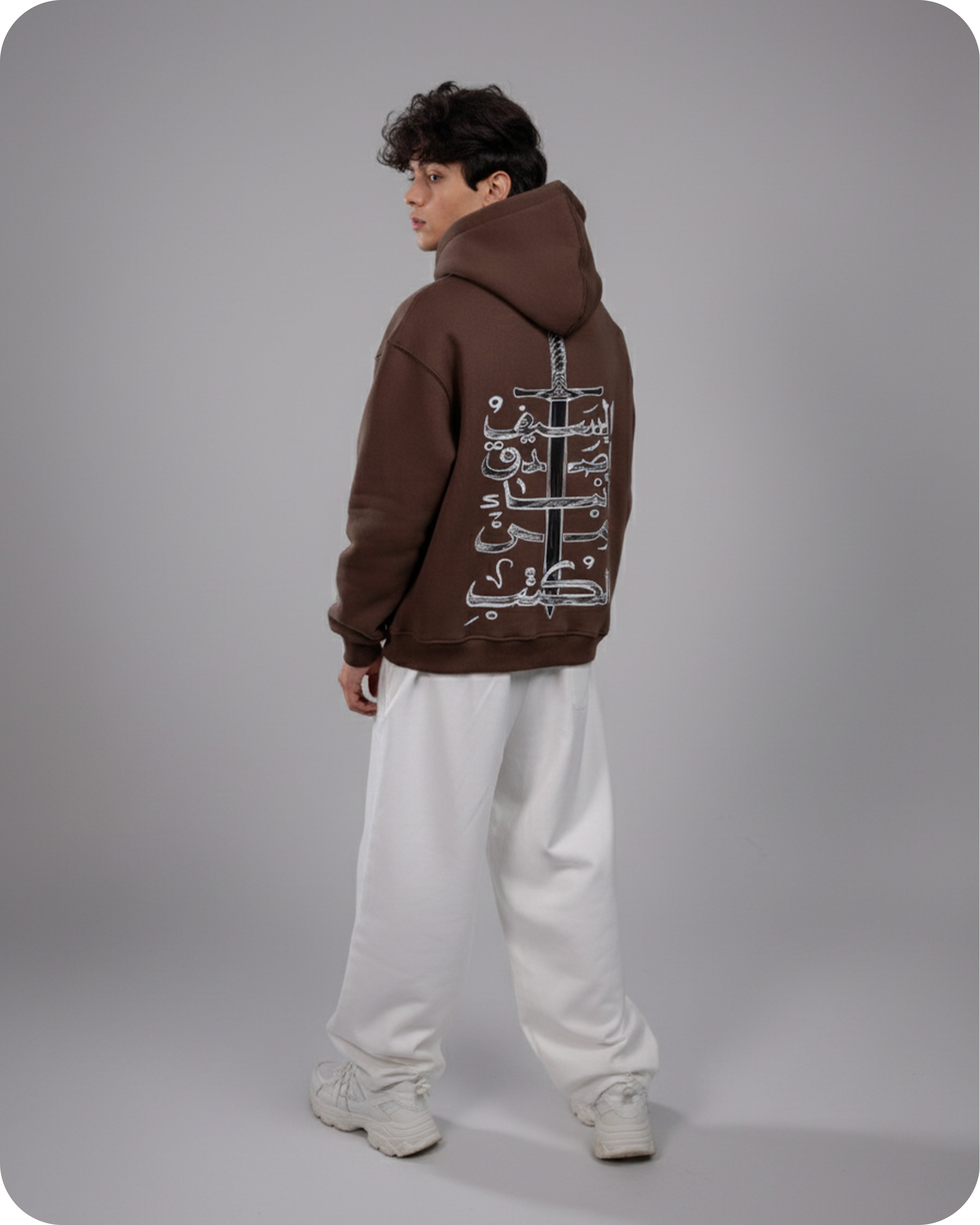 Person wearing a brown hoodie with Arabic text on the back against a gray background