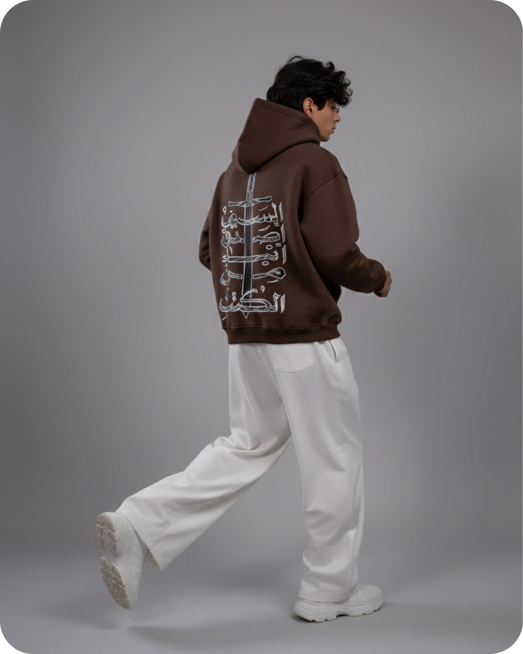 Person wearing a brown hoodie with white graphics on the back, standing against a gray background