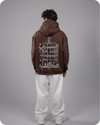 Person wearing a brown hoodie with white designs on the back against a gray background