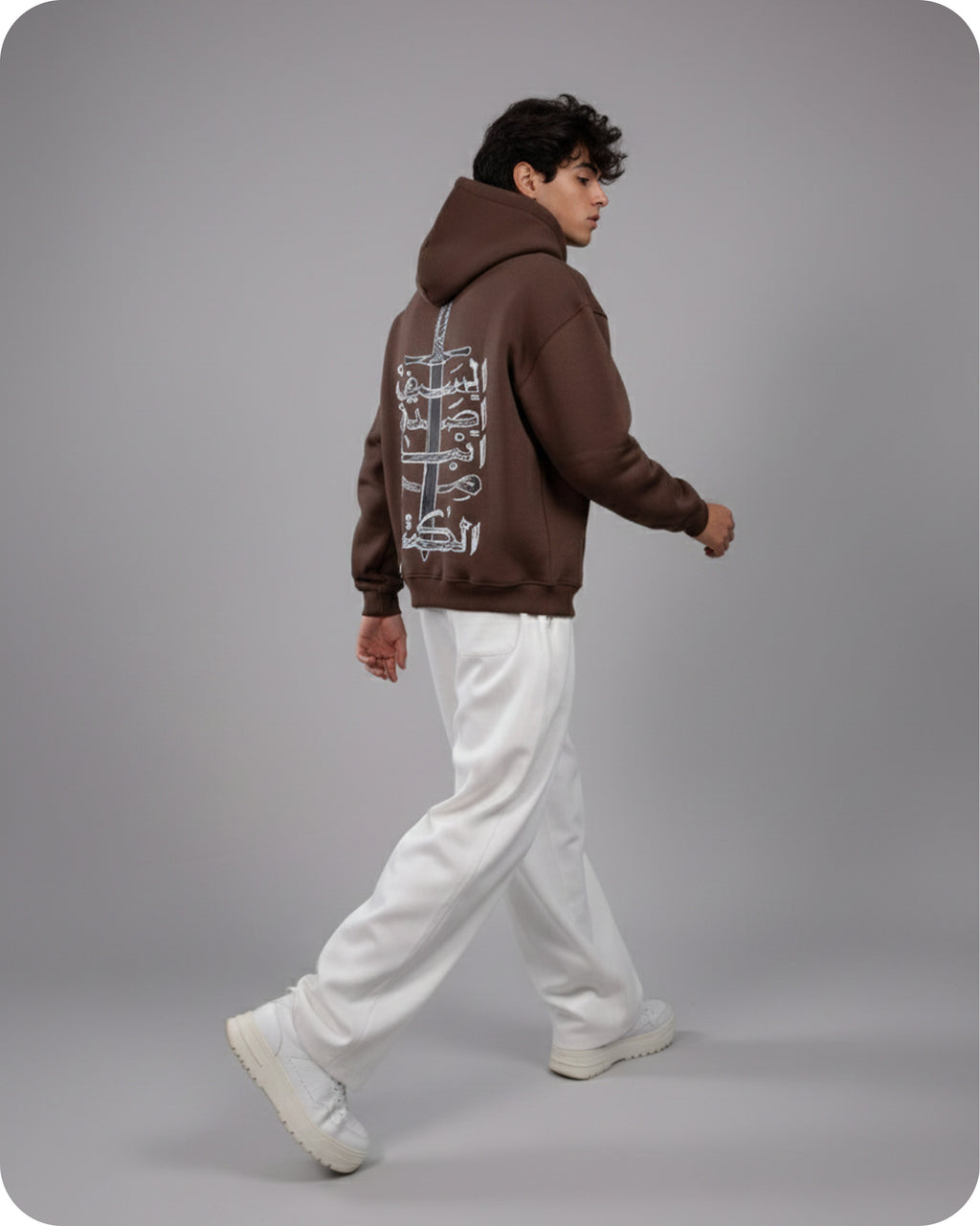 Person wearing a brown hoodie with a graphic design on the back, walking on a gray background