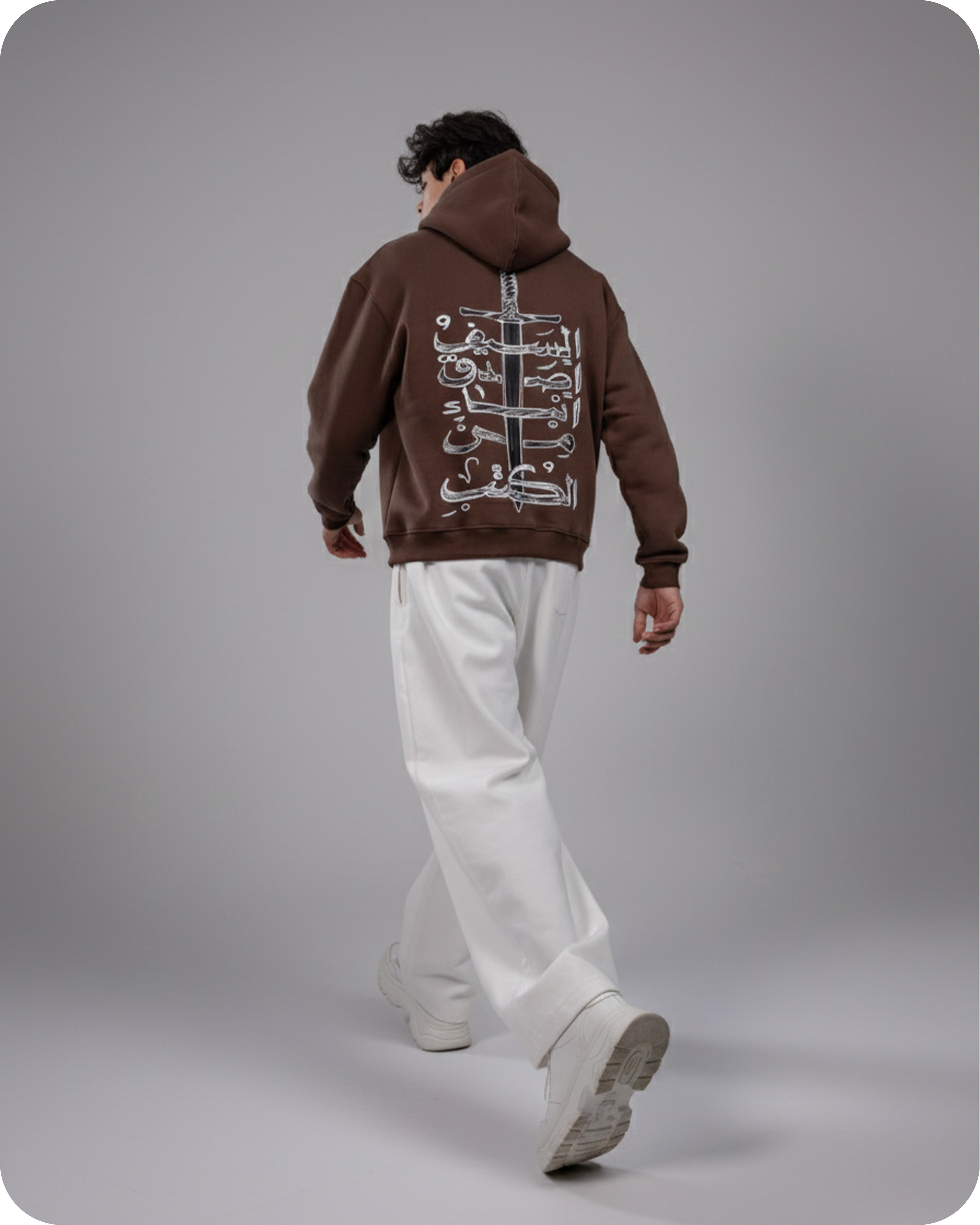 Person wearing a brown hoodie with Arabic text on the back, walking away on a plain background