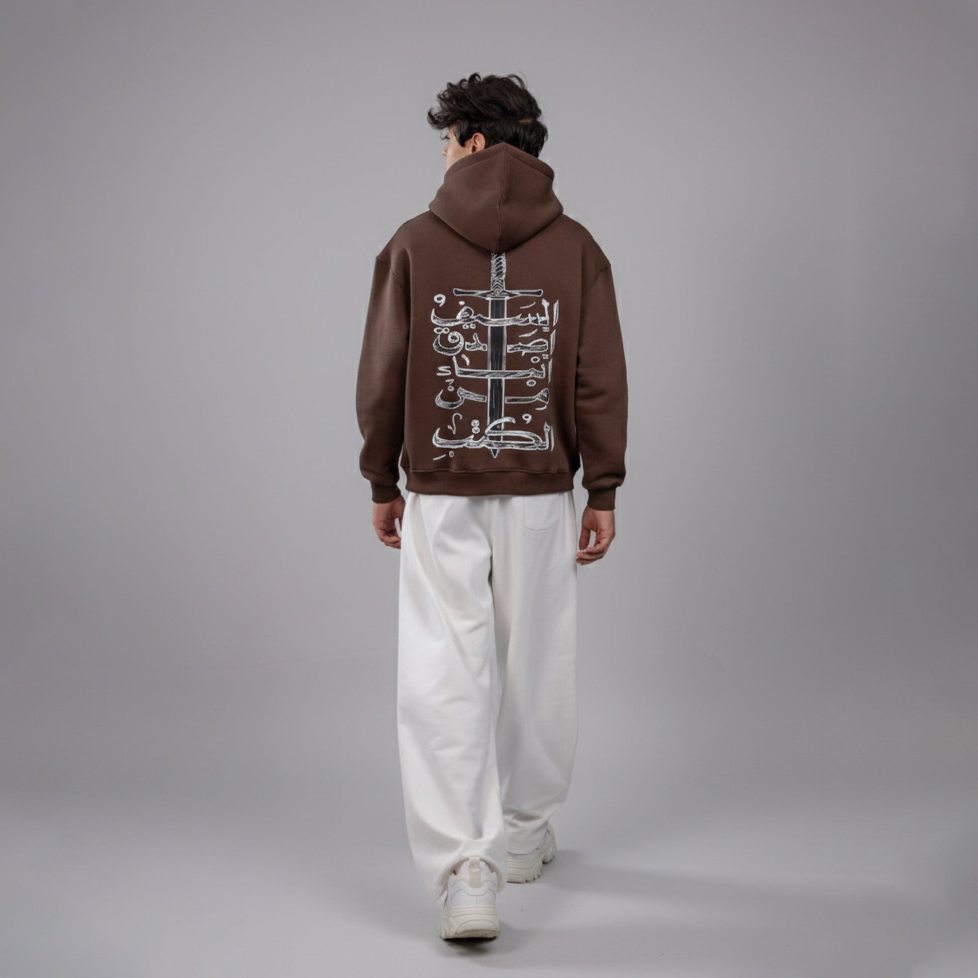 Person wearing a brown hoodie with a design on the back against a gray background