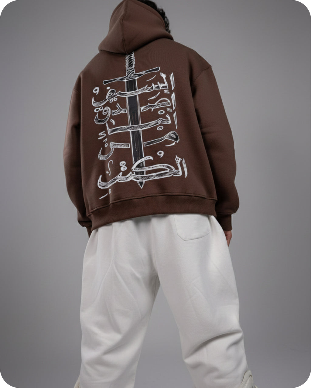 Person wearing a brown hoodie with Arabic text on the back against a gray background