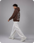 Person wearing a brown hoodie with white text and white pants on a gray background