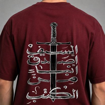 A close-up of a person's back wearing a maroon t-shirt with a large graphic print of a black sword and white Arabic calligraphy.
