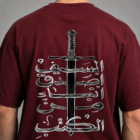 A close-up of a person's back wearing a maroon t-shirt with a large graphic print of a black sword and white Arabic calligraphy.
