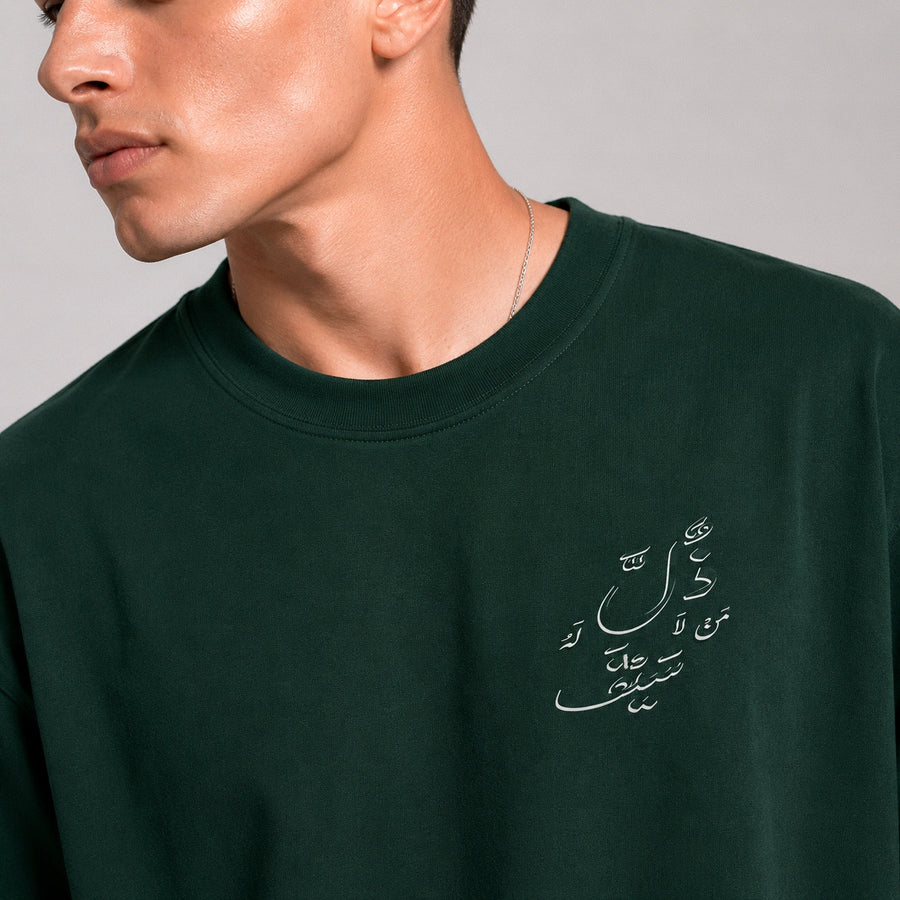Person wearing a dark green sweatshirt with Arabic text on a plain background