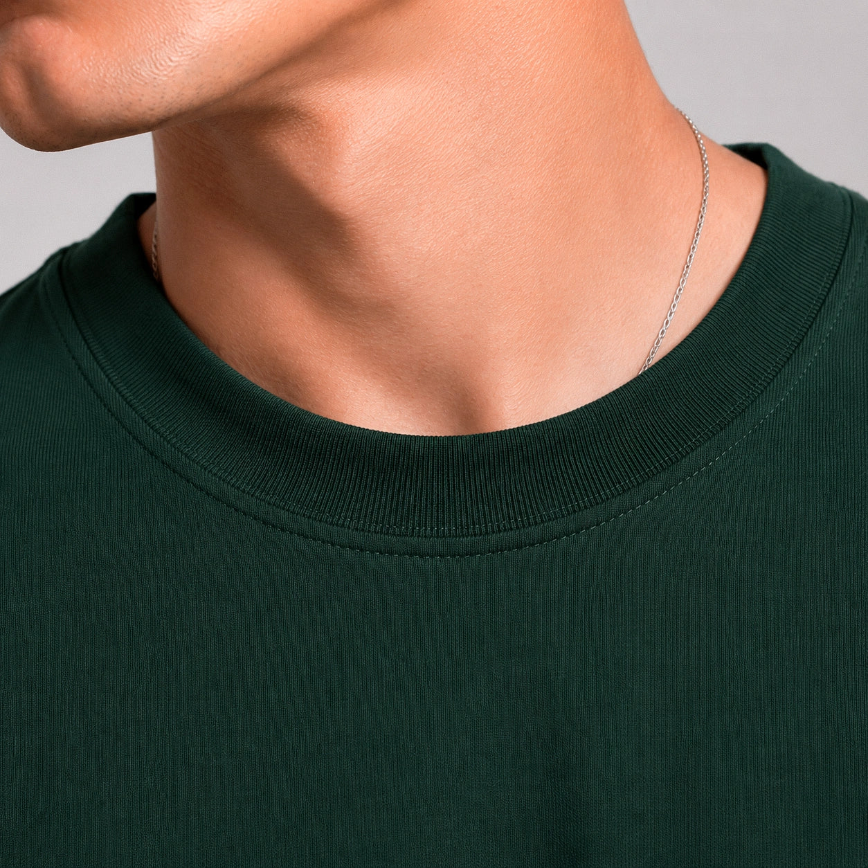 Close-up of a person wearing a dark green shirt with a plain background