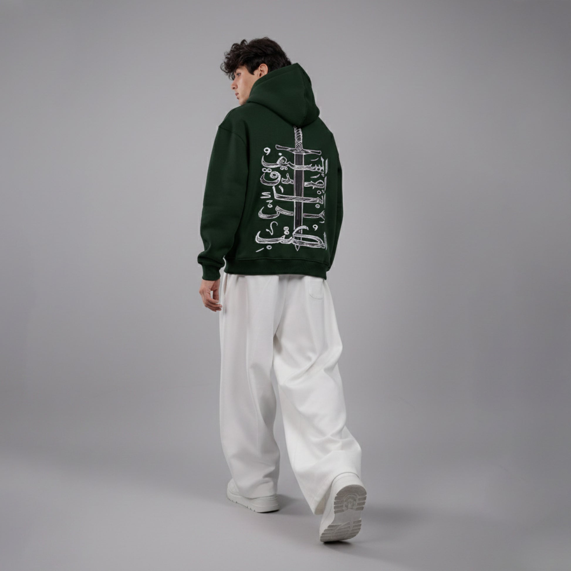 Person wearing a green hoodie with white text on the back, standing against a gray background