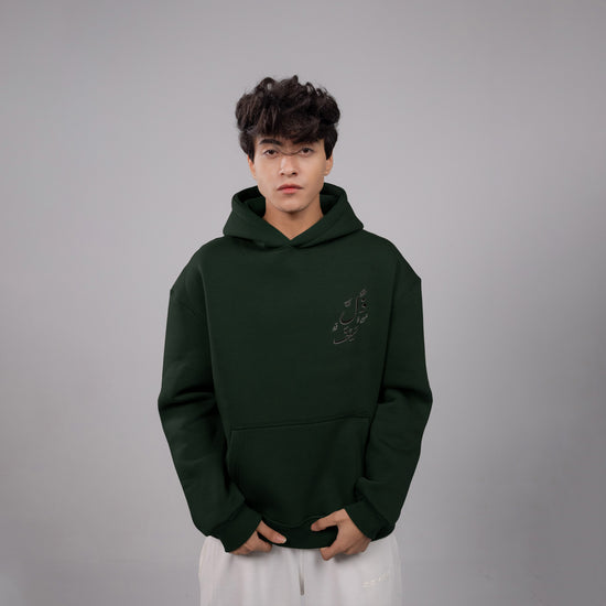 Person wearing a dark green hoodie with a small logo on a gray background