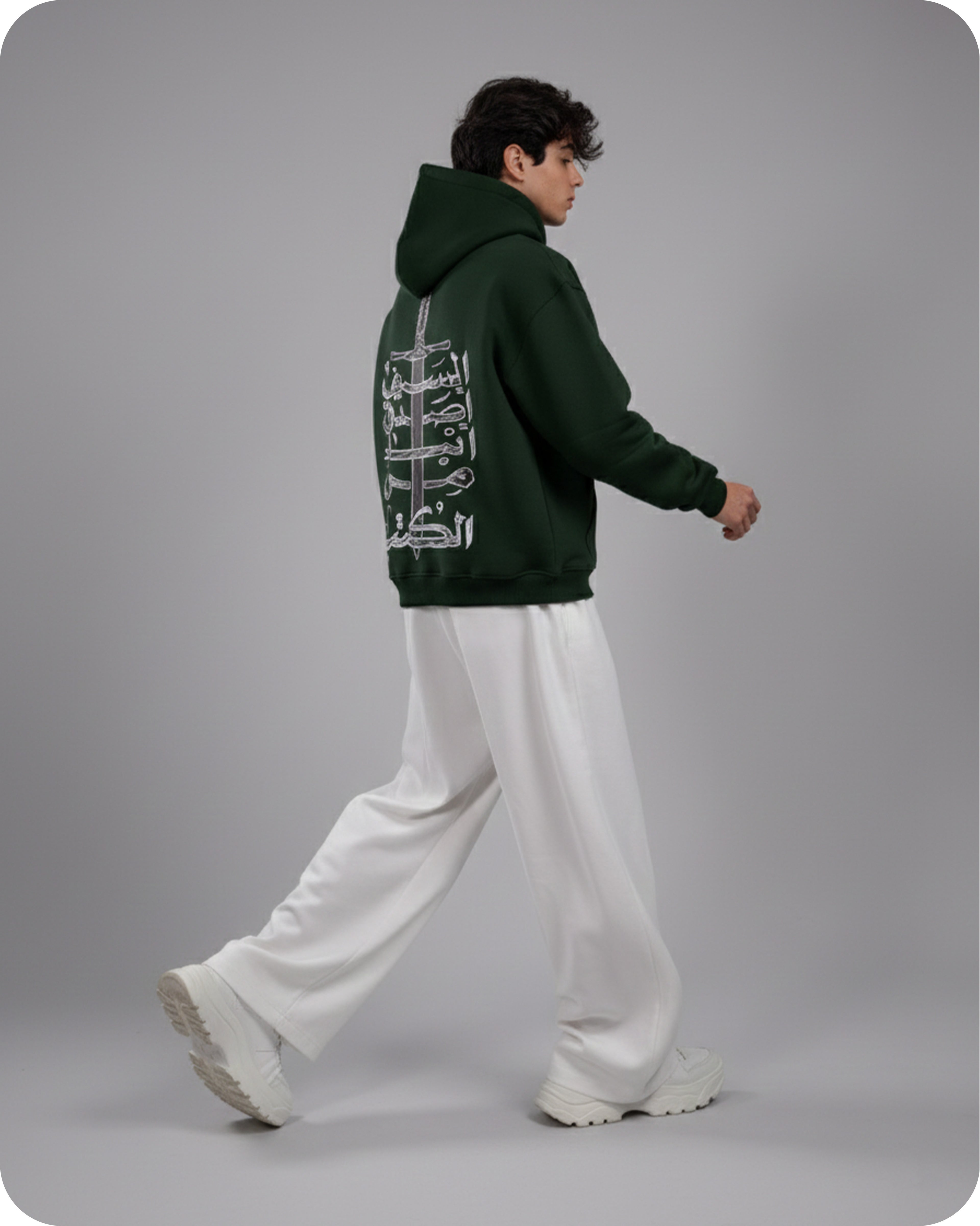 Person wearing a green hoodie with white designs on the back, standing against a gray background