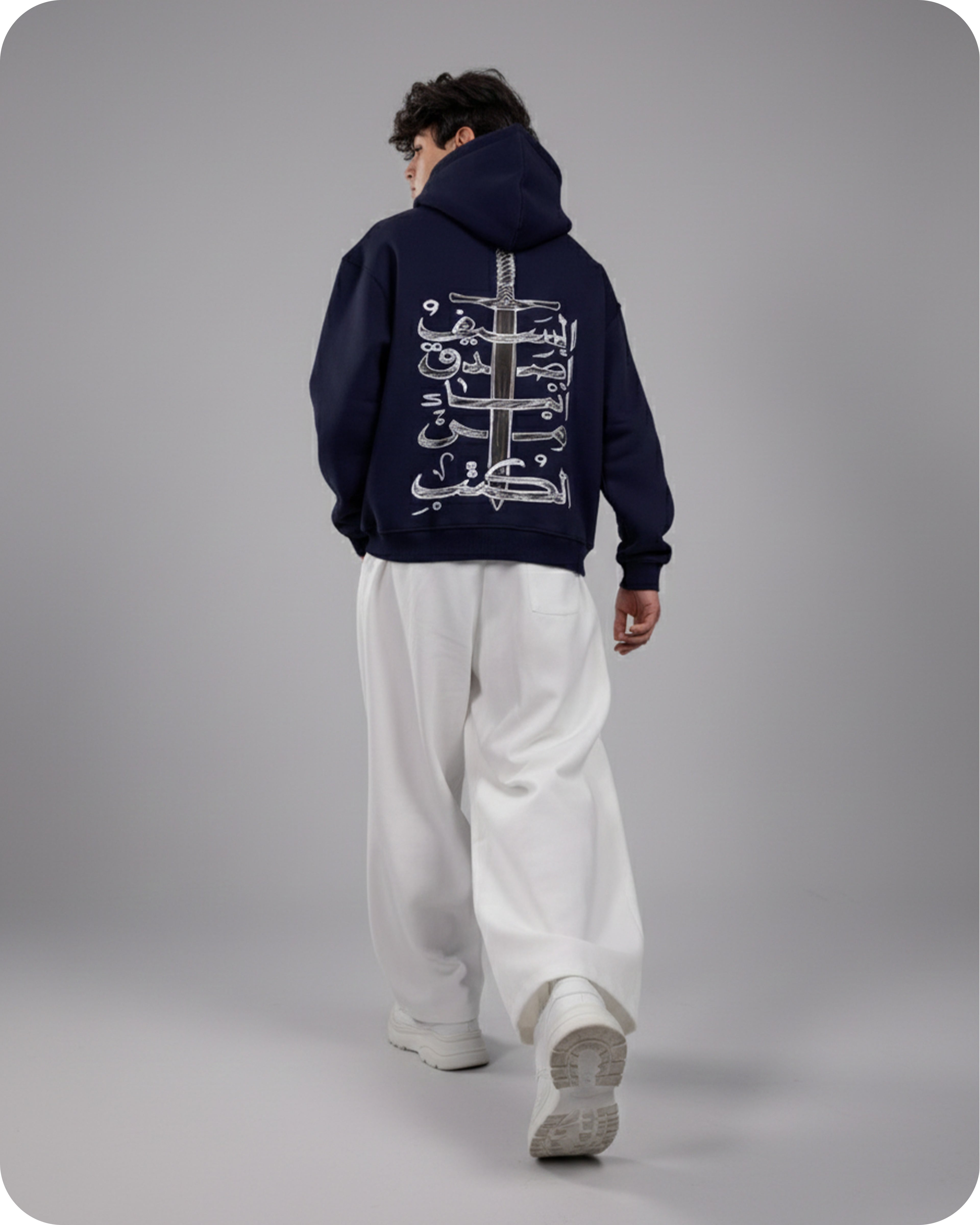 Person wearing a dark blue hoodie with white text and graphics on the back, standing against a gray background.