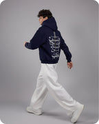 Person wearing a navy hoodie with a white graphic on the back, walking on a gray background